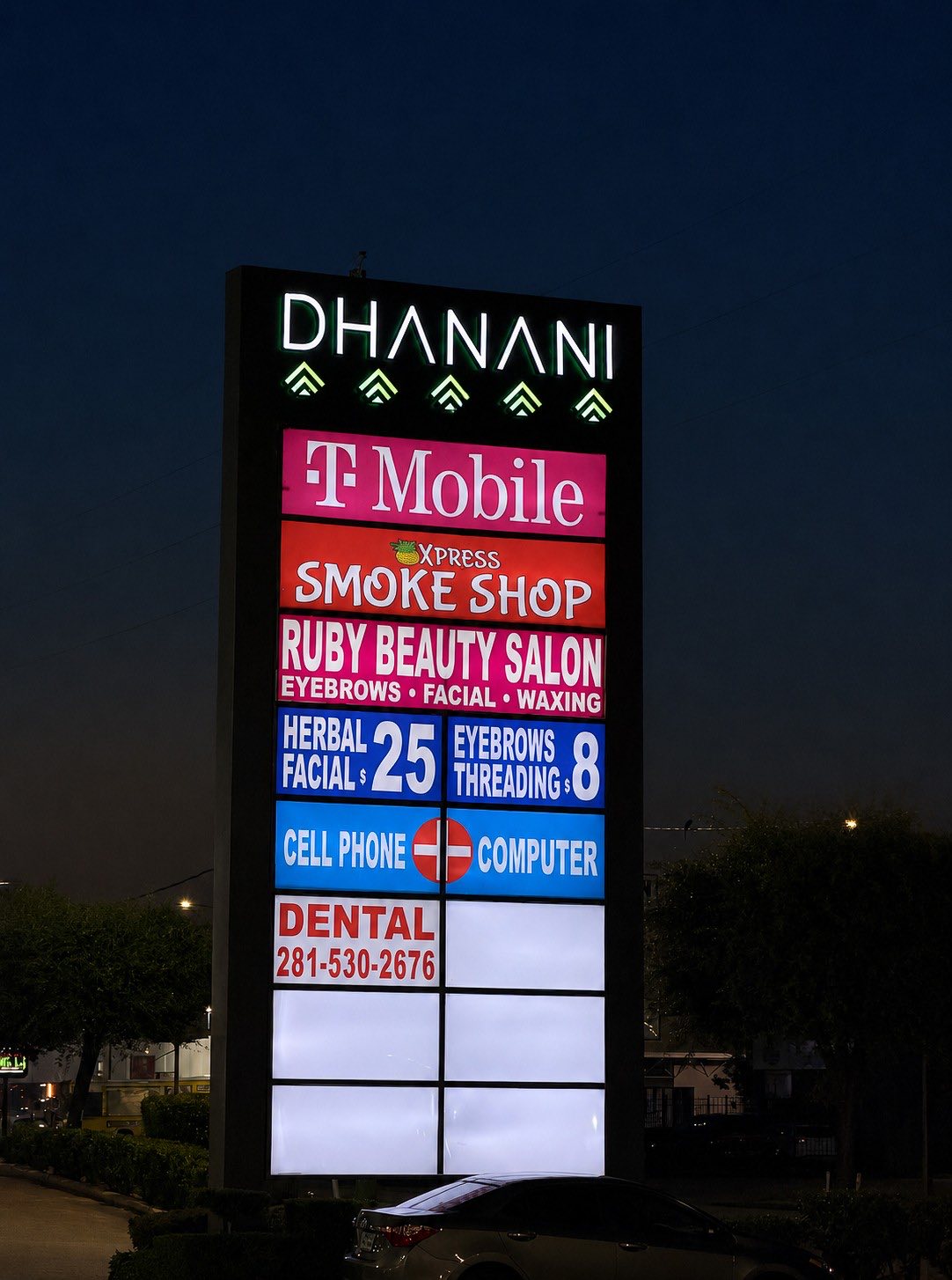 Illuminated Dhanani Plaza pylon sign listing every tenant, at night